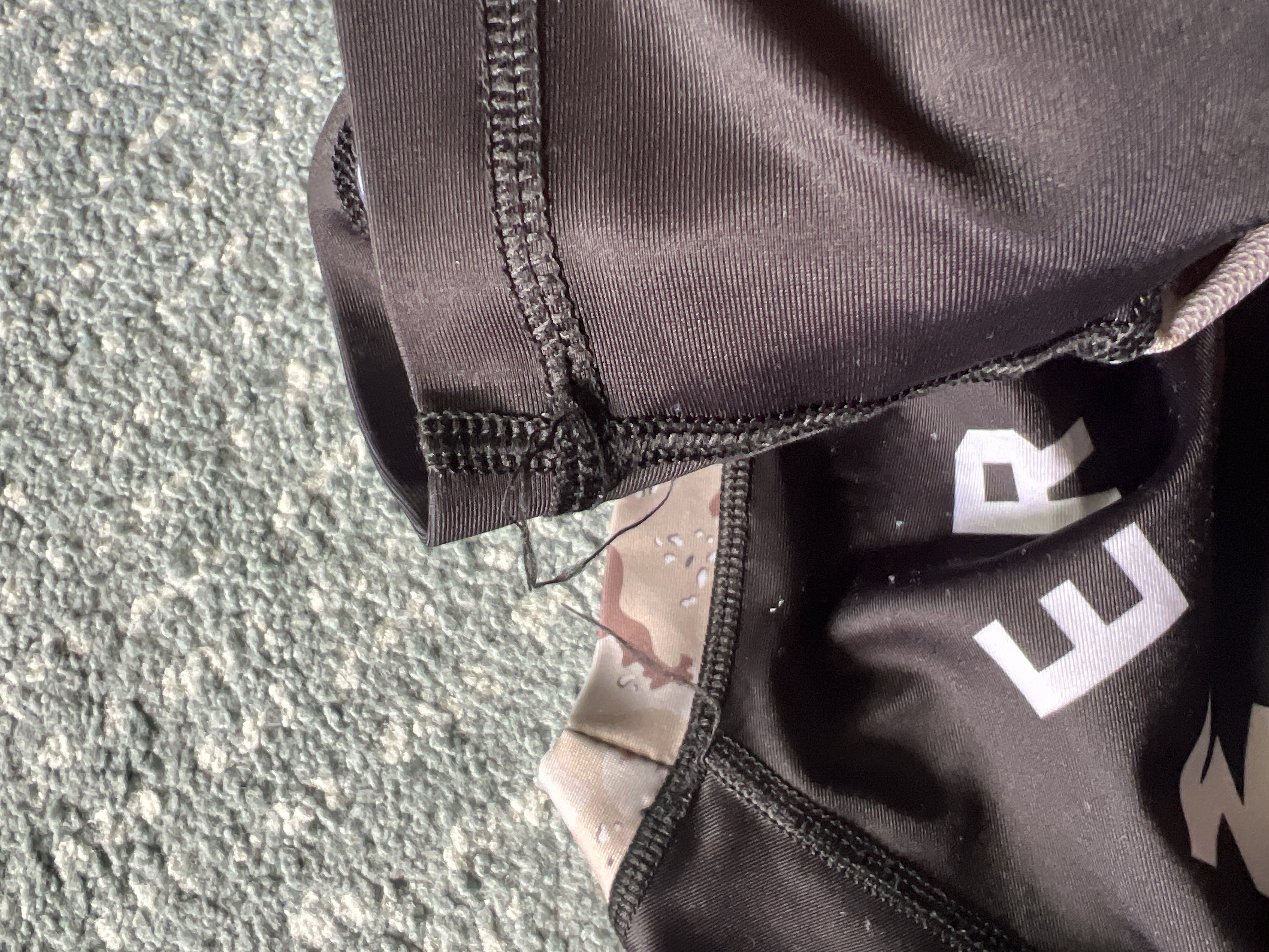 Macro view of loose threading at the collar and sleeve seams on the Level Black AJJ V2 rash guard